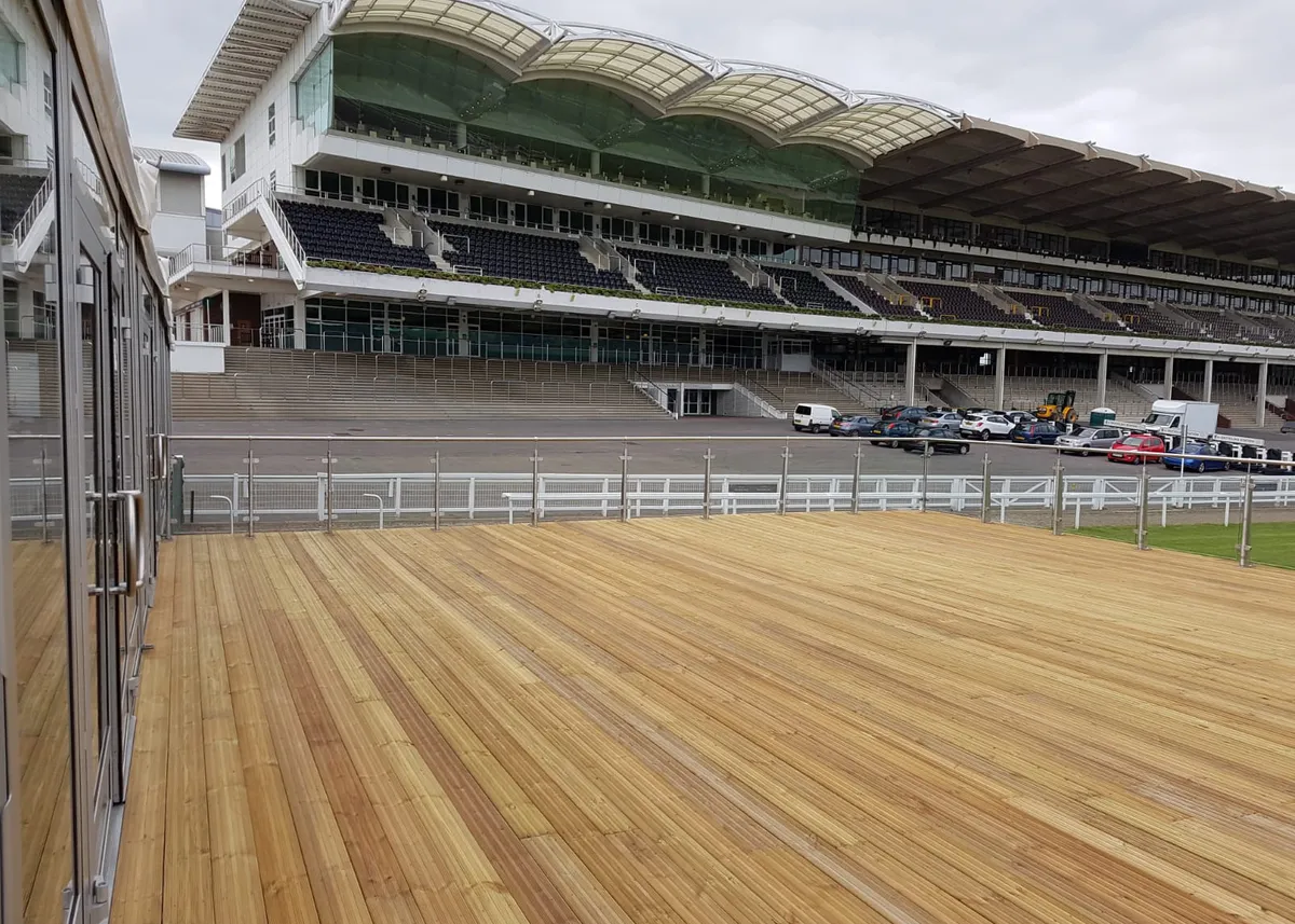 Timber decking platform overlooking a racecourse grandstand with seating and open event space