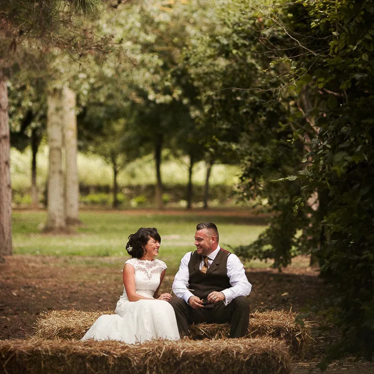 Bride and groom sitting on hay bales in a woodland wedding setting at The Tree Cathedral