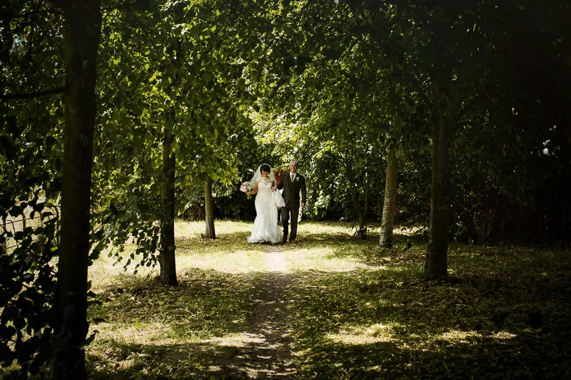 Bride and groom walking through a tree-lined path at The Tree Cathedral